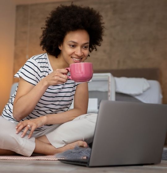 Woman having a coffee sitting on the floor and looking at a laptop screen
