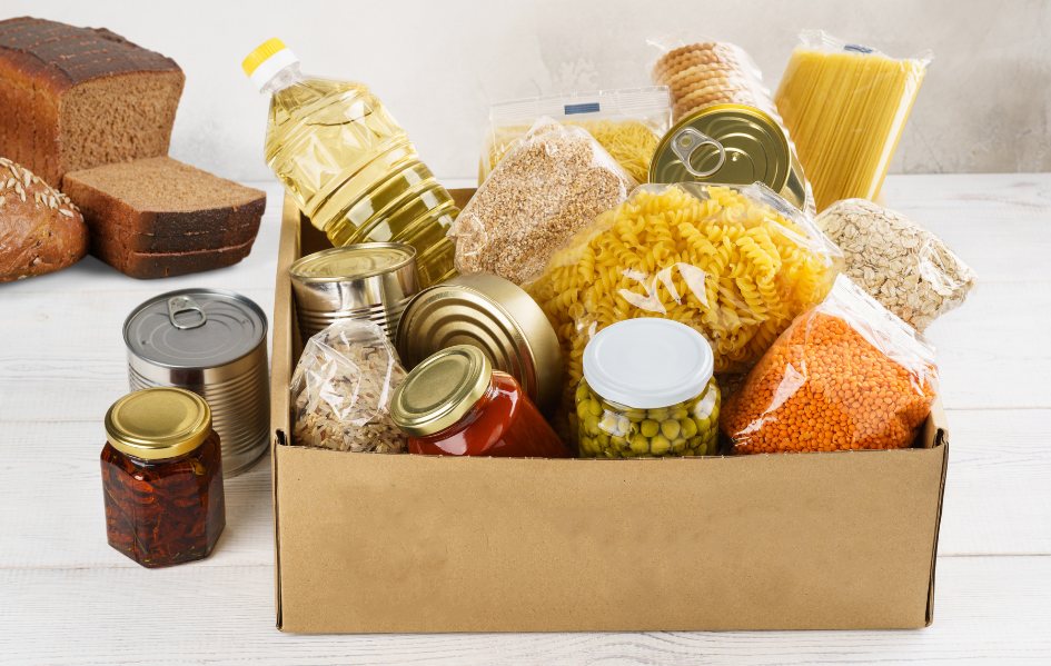 Box of food containing a variety of pasta, canned goods, cooking oils, breads and cereals.