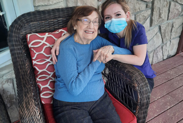 PSW wearing mask kneeling to hug smiling woman sitting in a chair.