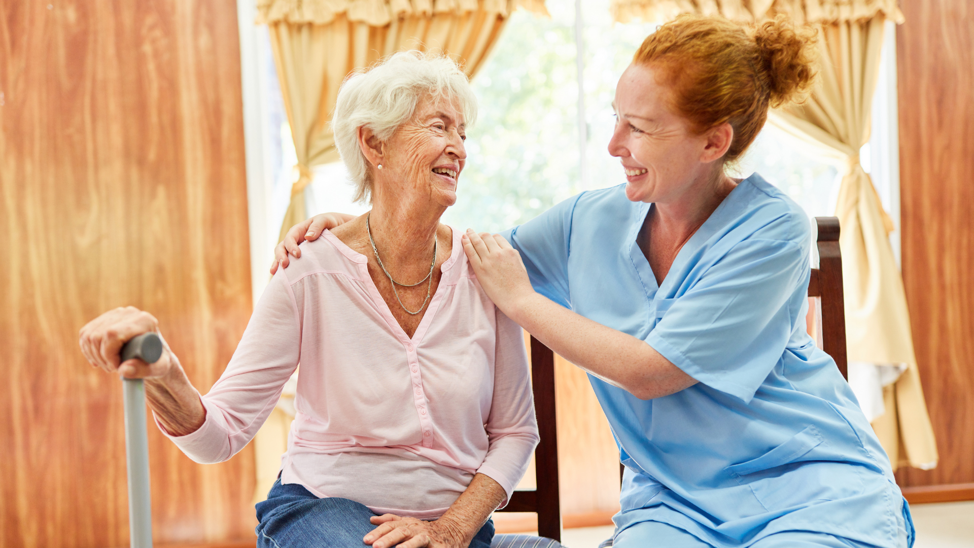 Smiling homecare provider sitting next to happy elderly woman