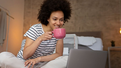 Woman sitting on floor enjoying a tea/coffee while watching her laptop
