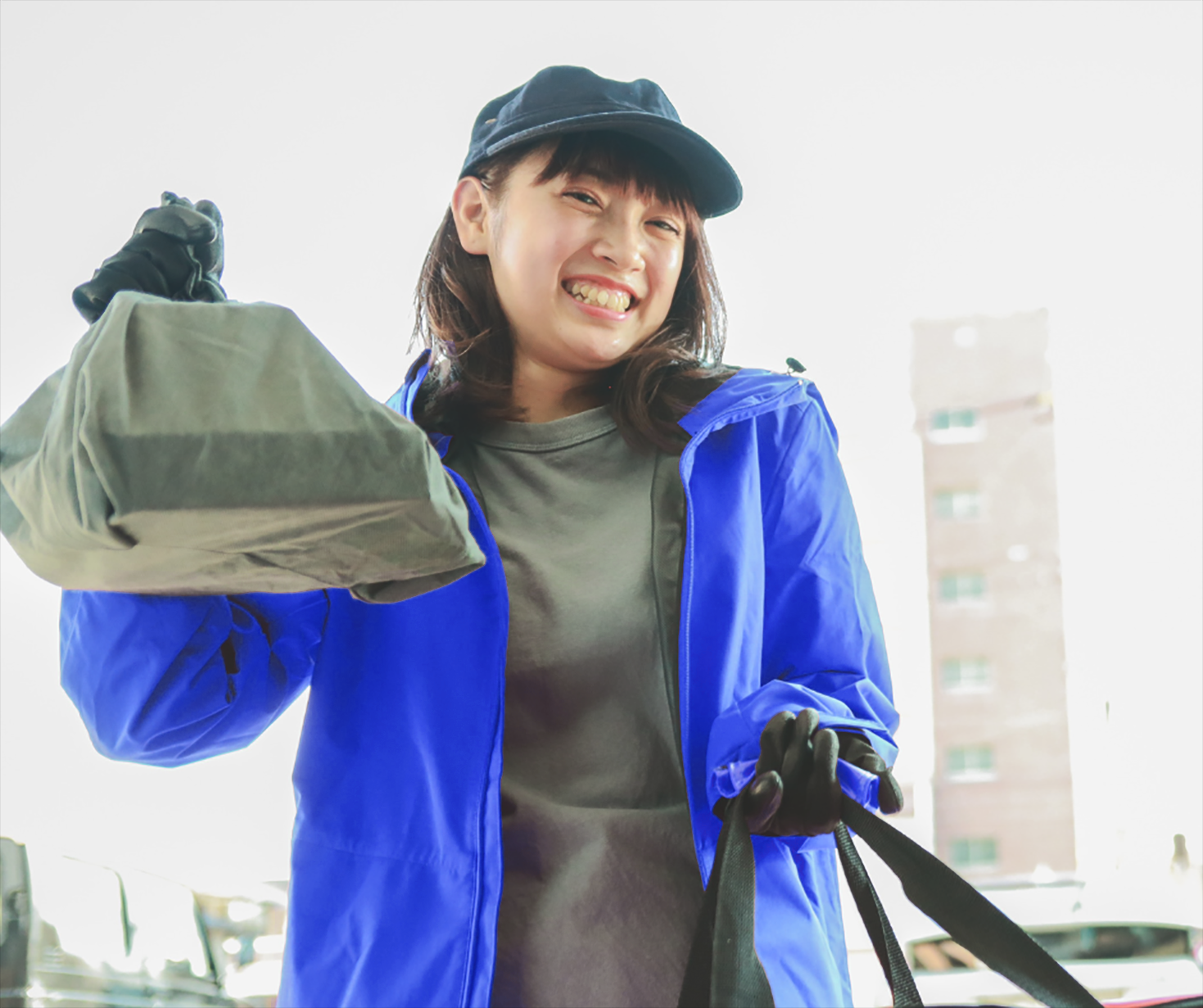 A female delivery person holds up a plastic bag with a delicious meal inside it at the front door.